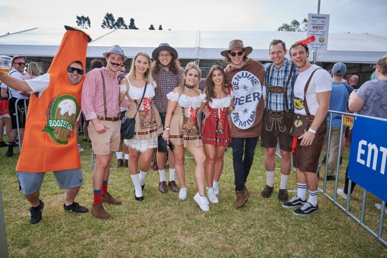 Group of people celebrating Oktoberfest wearing traditional Bavarian costumes, dirndls, and fun novelty outfits at an outdoor festival | MartyK Photography