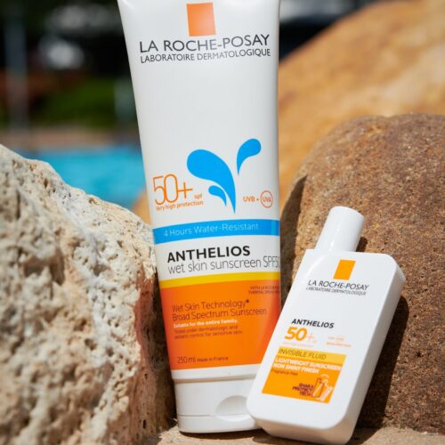La Roche-Posay Anthelios SPF 50+ sunscreen tube and bottle resting on rocks near a sunny beach | MartyK Photography